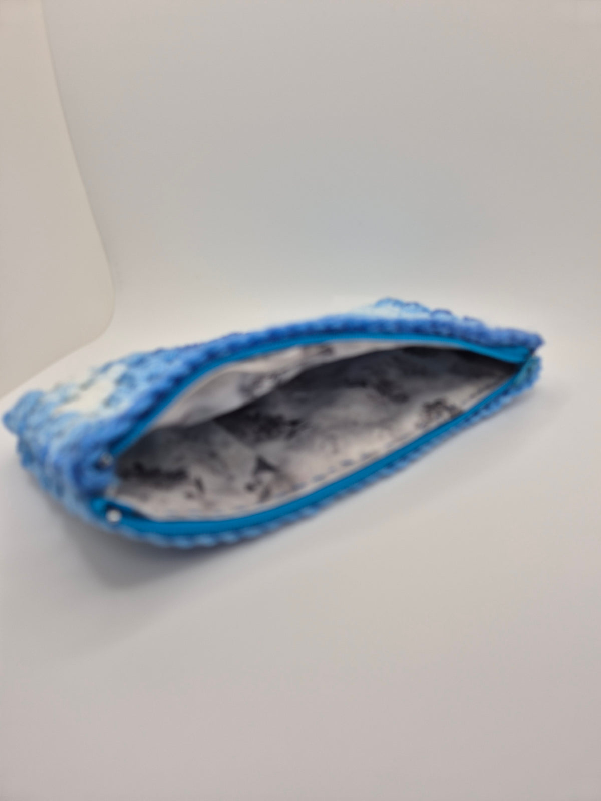 A small zippered pouch or cosmetic case with a blue fuzzy exterior and a gray-and-white marbled interior, photographed on a plain light background.